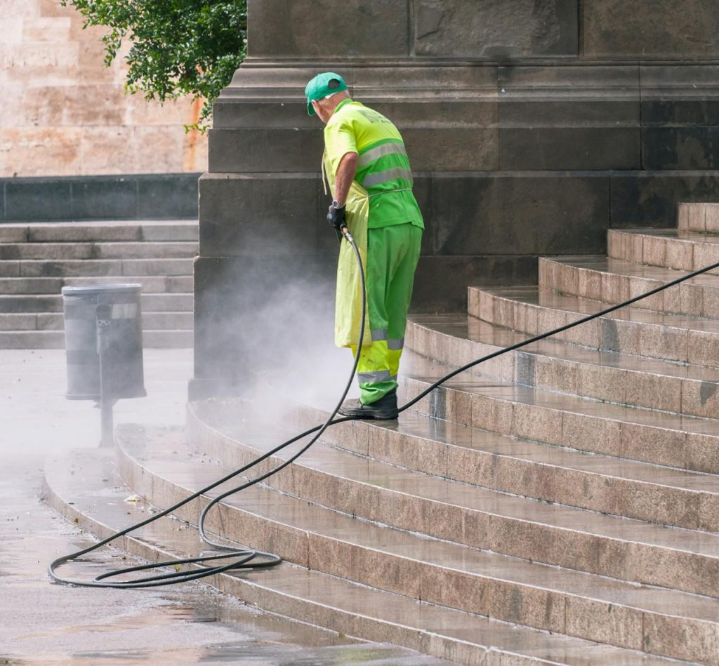 man-cleaning-stairs-on-street-14965464 A street worker pressure washes stone stairs in a public park, ensuring cleanliness and safety.